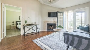 A living room with hardwood flooring, a fireplace, a sofa, a TV mounted on the wall, and a ceiling fan. - The Davis 1824 I Spacious 2 Bed 2 Bath (Huntsville)