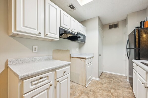 A kitchen with white cabinets, a stainless steel refrigerator, and a tiled floor.