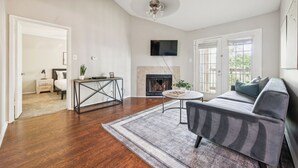 A living room with hardwood flooring, a gray sofa, a coffee table, a fireplace, and a TV mounted on the wall. - The Davis 1824 I Spacious 2 Bed 2 Bath (Huntsville)