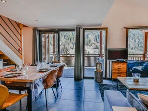 A dining area with a table set for four, a television, and a view of a mountainous landscape through large windows.