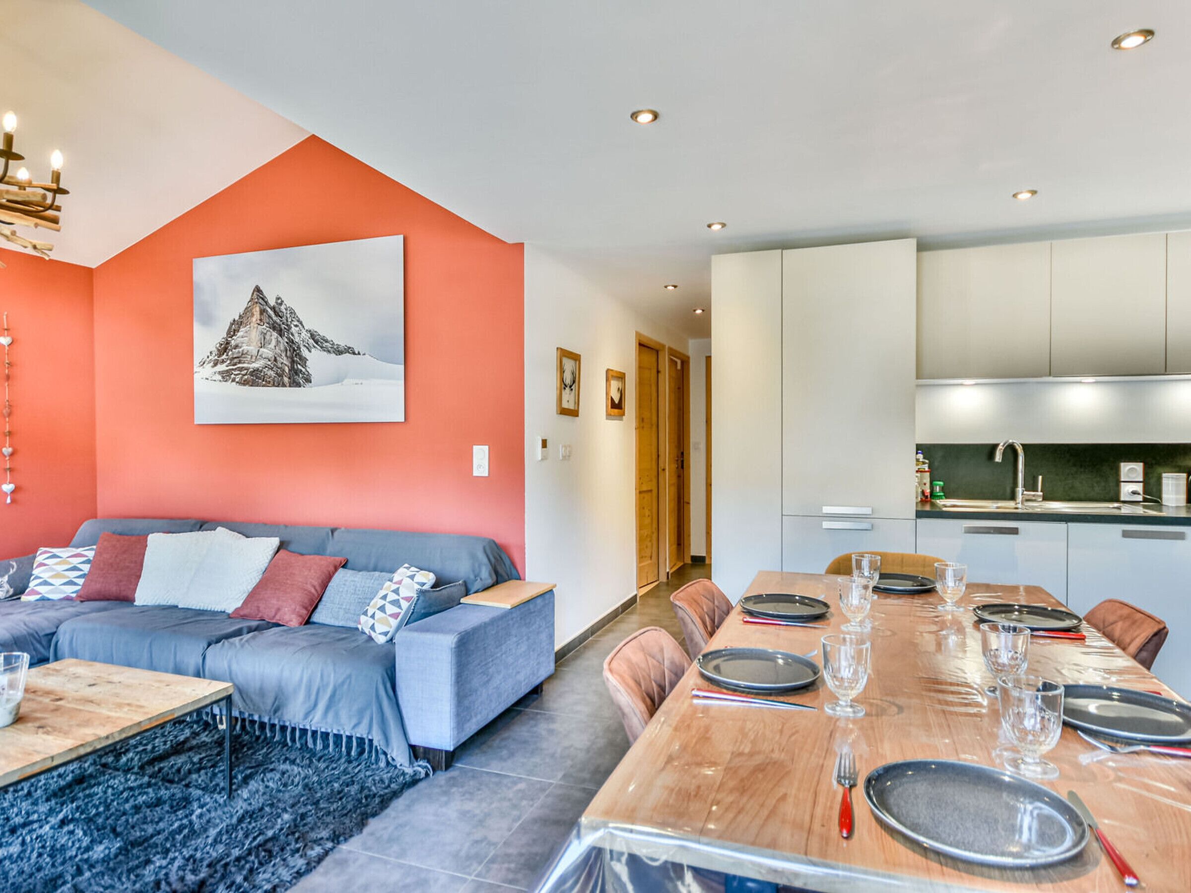 Una sala moderna con sofá, mesa de comedor lista para cuatro personas y una cocina con armarios y pileta.