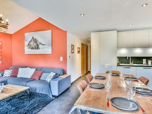 A modern living room with a sofa, dining table set for four, and a kitchen area with cabinets and a sink. - T4 Apartment in Les Gets - 6 to 8 people with Parking (Les Gets)