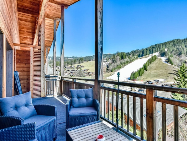 A wooden deck with wicker furniture and a clear view of a snowy mountain landscape.