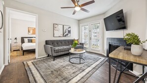 A modern living room with a grey sofa, a round coffee table, a ceiling fan, a flat-screen TV, and a fireplace.