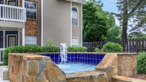 A stone pool with a waterfall feature, surrounded by a stone wall and a wooden fence.