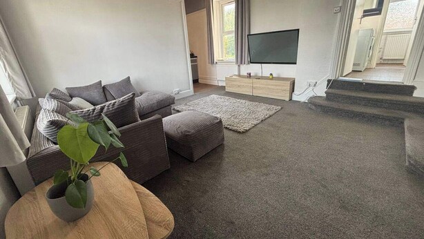 Una sala de estar moderna con un sofá gris, un televisor de pantalla plana y una escalera que sube a un piso superior.