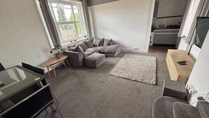Un espacio habitable compacto con un sofá, una mesita, un televisor y una zona de cocina.