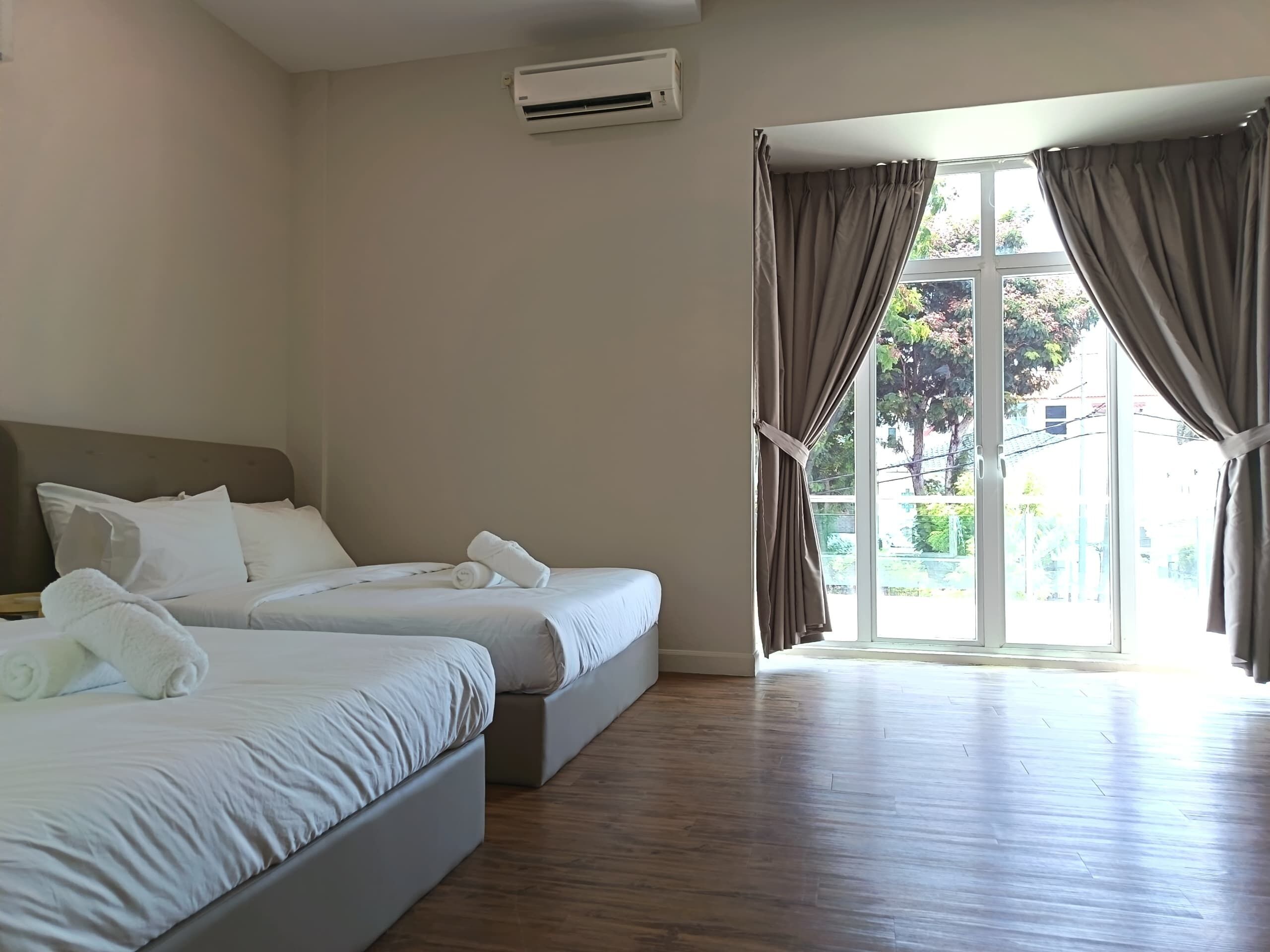 A hotel room with two beds, a large window with curtains, and an air conditioning unit.
