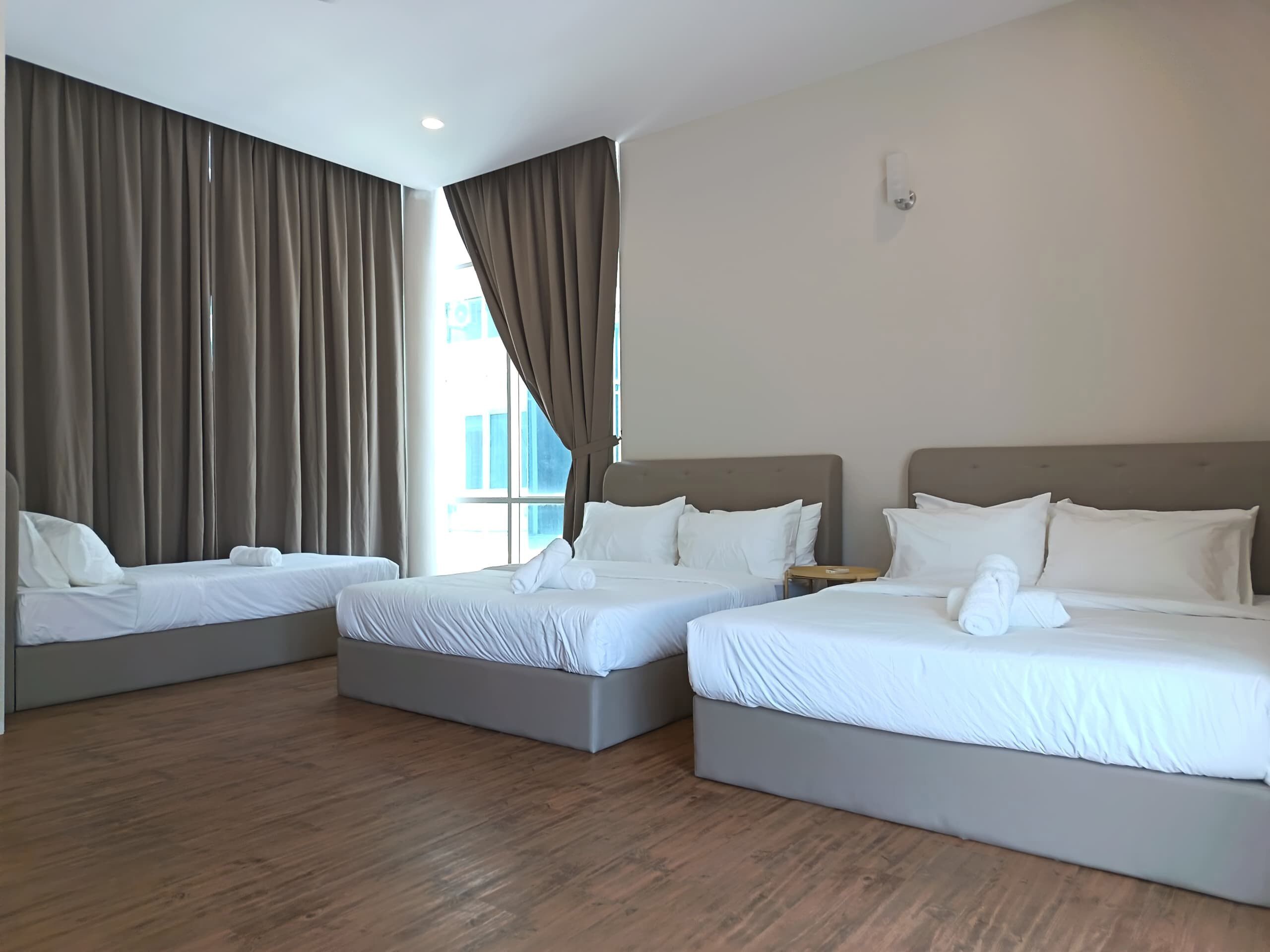Ein Hotelzimmer mit drei Einzelbetten, Holzboden und großen Fenstern mit Vorhängen.