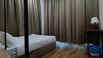 Ein Hotelzimmer mit Bett, Vorhängen, einem Nachttisch mit Lampe und einem Papierkorb.