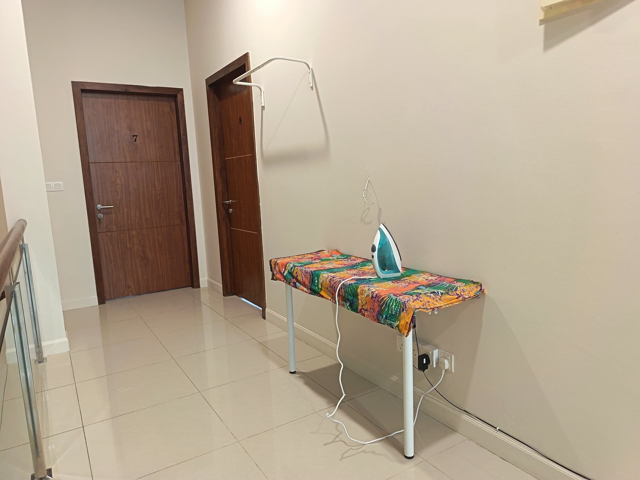 A room with a wooden door, a white ironing board with an iron, and a tiled floor.