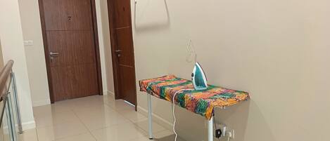 A room with a wooden door, a white ironing board with an iron, and a tiled floor.