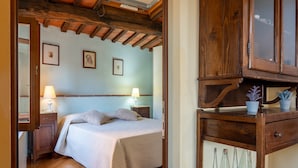 A bedroom with a wooden bed, bedside lamps, a wooden nightstand, and a wooden cabinet with glass bottles. - Apartment 'Piccolo Rustico' with Mountain View, Wi-Fi and Air Conditioning (Scrofiano)