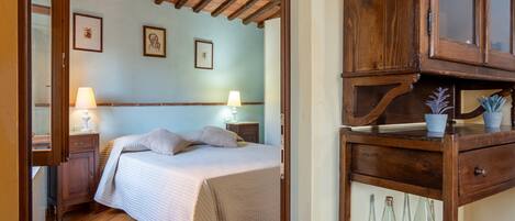 A bedroom with a wooden bed, bedside lamps, a wooden nightstand, and a wooden cabinet with glass bottles.