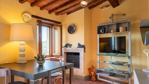 A cozy living room with a fireplace, a television on a glass shelf, and a dining area with a table and chairs. - Apartment 'Piccolo Rustico' with Mountain View, Wi-Fi and Air Conditioning (Scrofiano)