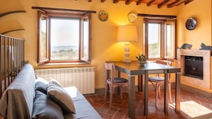 A cozy room with a wooden ceiling, a dining table with chairs, a sofa, a fireplace, and large windows with a view. - Apartment 'Piccolo Rustico' with Mountain View, Wi-Fi and Air Conditioning (Scrofiano)