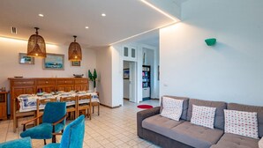 Ein modernes Wohnzimmer mit einer Couch, Sesseln, einem Esstisch und Pendelleuchten.