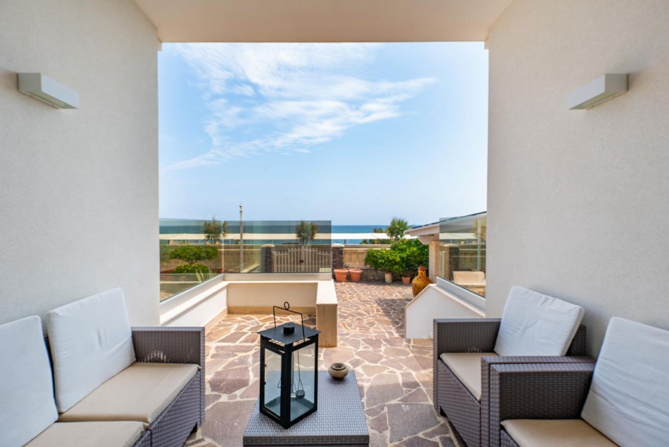 A balcony with wicker furniture, a glass table, and a view of the sea.