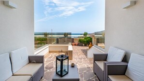 Ein Balkon mit Korbmöbeln, einem Glastisch und Blick aufs Meer.