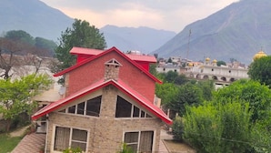 A two-story building with a red roof, surrounded by lush greenery and mountains in the background. - Hotel Himalaya (Bhuntar)