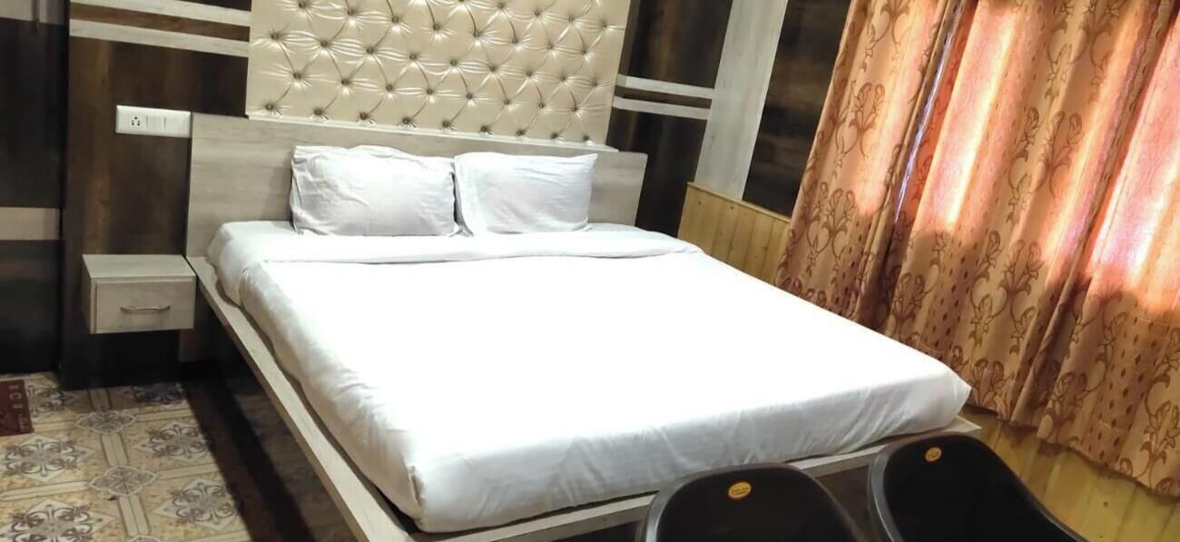 A neatly made bed with white linens, a tufted headboard, a bedside table with a drawer, and a patterned rug on the floor.
