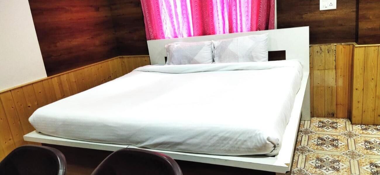 Uma cama de solteiro com colchão e almofadas brancas, cabeceira de madeira e piso estampado.