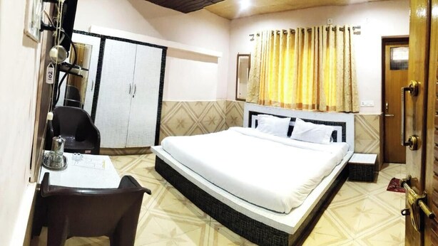 A bedroom with a bed, a desk, a chair, a wardrobe, and a bathroom with a curtain. - Hotel Himalaya (Bhuntar)