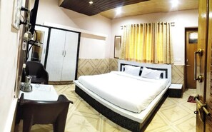 A bedroom with a bed, a desk, a chair, a wardrobe, and a bathroom with a curtain. - Hotel Himalaya (Bhuntar)