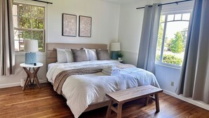 Een slaapkamer met een bed, nachtkastjes, een plafondventilator en een raam met gordijnen.
