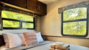 Une chambre à coucher avec un lit, des oreillers, une couverture et une fenêtre donnant sur des arbres.