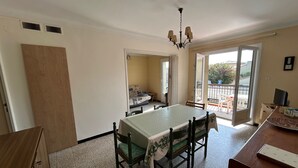 A dining area with a table and chairs, a wooden cabinet, a ceiling light fixture, and a view of an outdoor balcony.