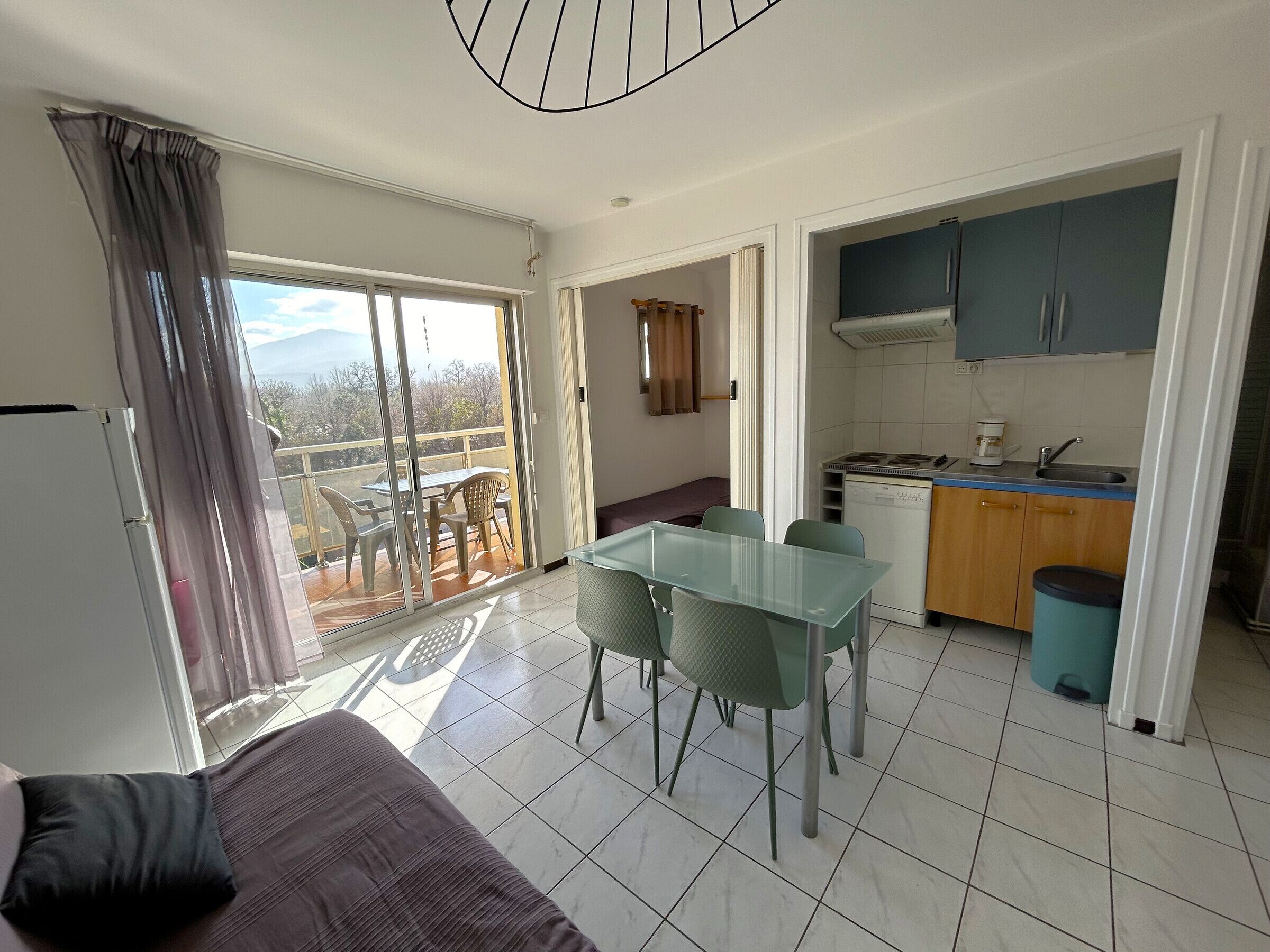 A room with a balcony, a dining area, and a kitchenette.