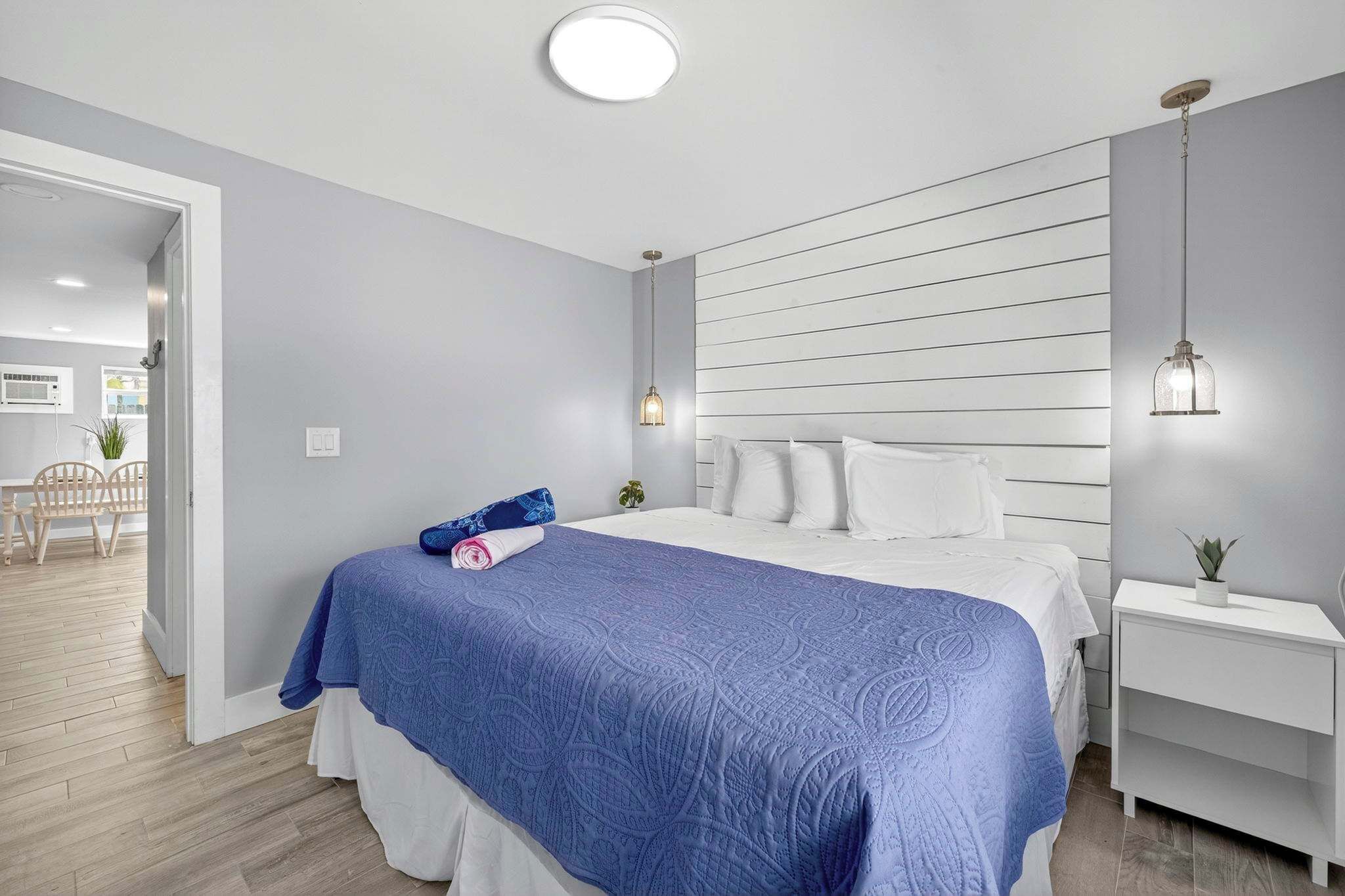 A bedroom with a bed, a bedside table, a nightstand, and a wall-mounted light fixture.