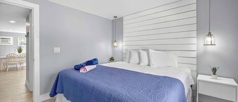 A bedroom with a bed, a bedside table, a nightstand, and a wall-mounted light fixture.