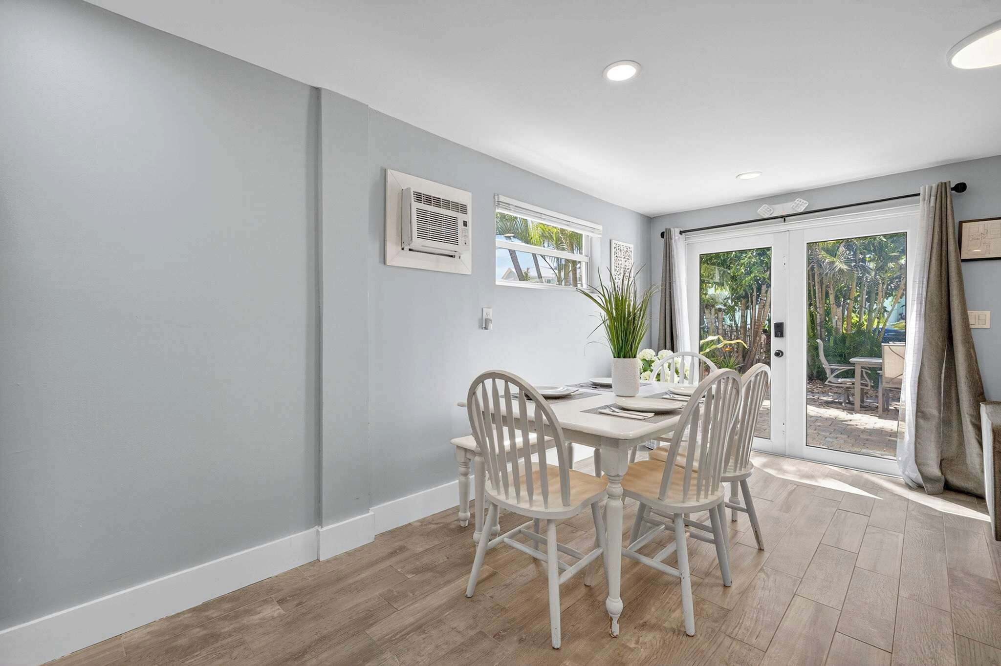 A dining area with a table and four chairs, a potted plant, and a view of the outdoors through a glass door.