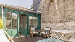 A wooden deck with a green door, a stone wall, and outdoor furniture including a table and chairs. - Charming duplex with private terrace in the heart of Avranches (Avranches)
