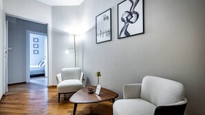 Un salon moderne avec un plancher en bois, deux fauteuils blancs, une petite table ronde avec une lampe et deux œuvres d’art encadrées accrochées au mur.