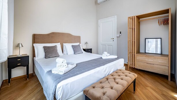 Une chambre d’hôtel bien aménagée, avec un lit, des tables de chevet, un banc, une armoire et une fenêtre donnant sur un beau paysage.