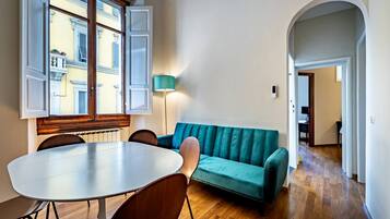 Une pièce comprenant une table à manger, des chaises, un canapé de couleur turquoise et une lampe.