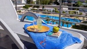 Eine Liege mit blauem Handtuch, einer Flasche Astroturf, einem Glas, einem Buch und einem Apfel auf einem Tablett.