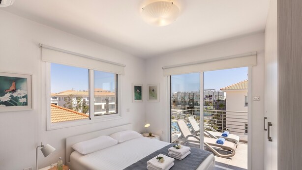 Ein modernes Schlafzimmer mit Bett, Nachttisch und Blick auf einen Pool und Gebäude.
