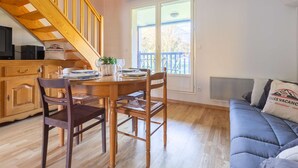 A dining area with a wooden table, chairs, and a chandelier. A staircase leads to an upper level.
