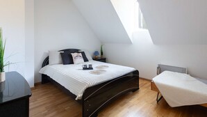 A bedroom with a sloped ceiling, a bed with a white bedspread, a bedside table with a lamp, and a small bedside plant.