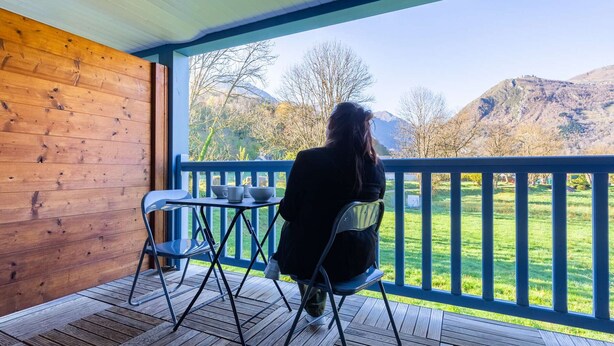 A wooden deck with a table and chairs, overlooking a grassy area with mountains in the background.