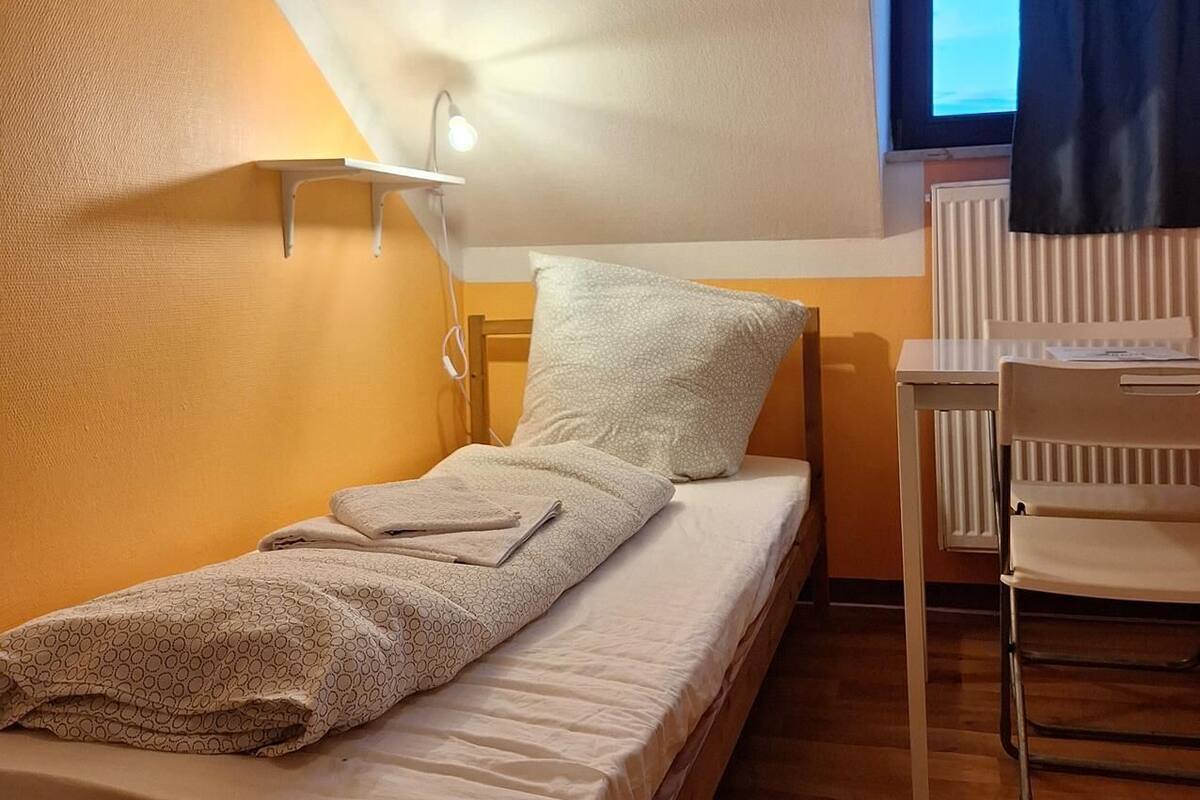 Une petite pièce agréable, dotée d’un lit simple, d’un bureau et d’une fenêtre avec des rideaux.