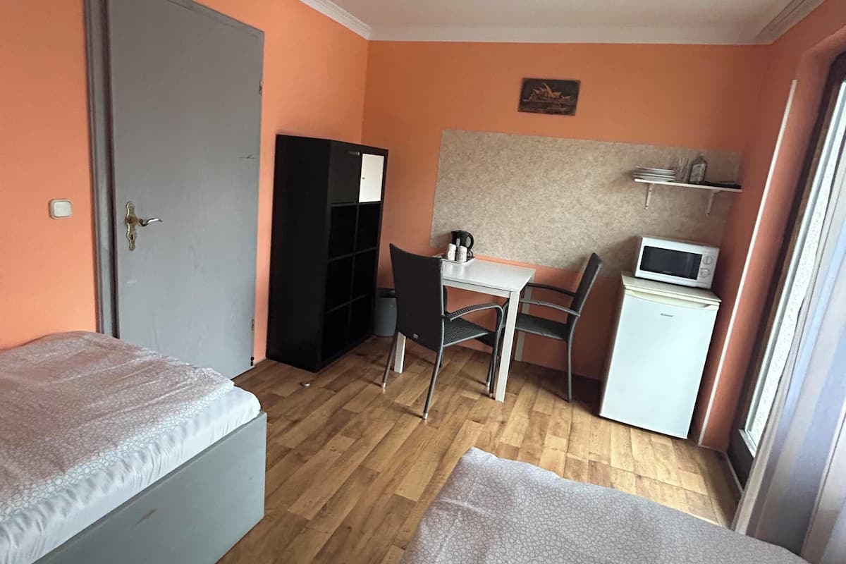 Une chambre compacte comprenant deux lits, un bureau, une chaise, un four à micro-ondes et un petit réfrigérateur.