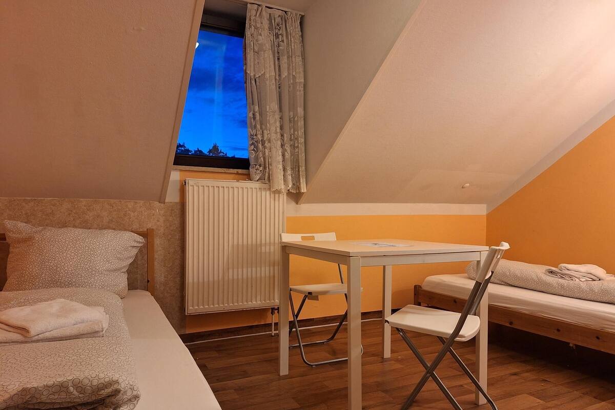 Une petite pièce agréable et confortable, avec un lit, un bureau et une chaise. Il y a une fenêtre avec des rideaux, un radiateur et une vue sur le ciel.