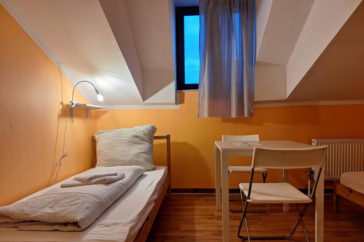 Une petite pièce bien éclairée, avec un lit, un bureau et une chaise.