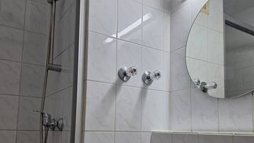 Une salle de bain équipée d’une douche, d’un lavabo, d’un miroir et d’un distributeur de savon liquide.