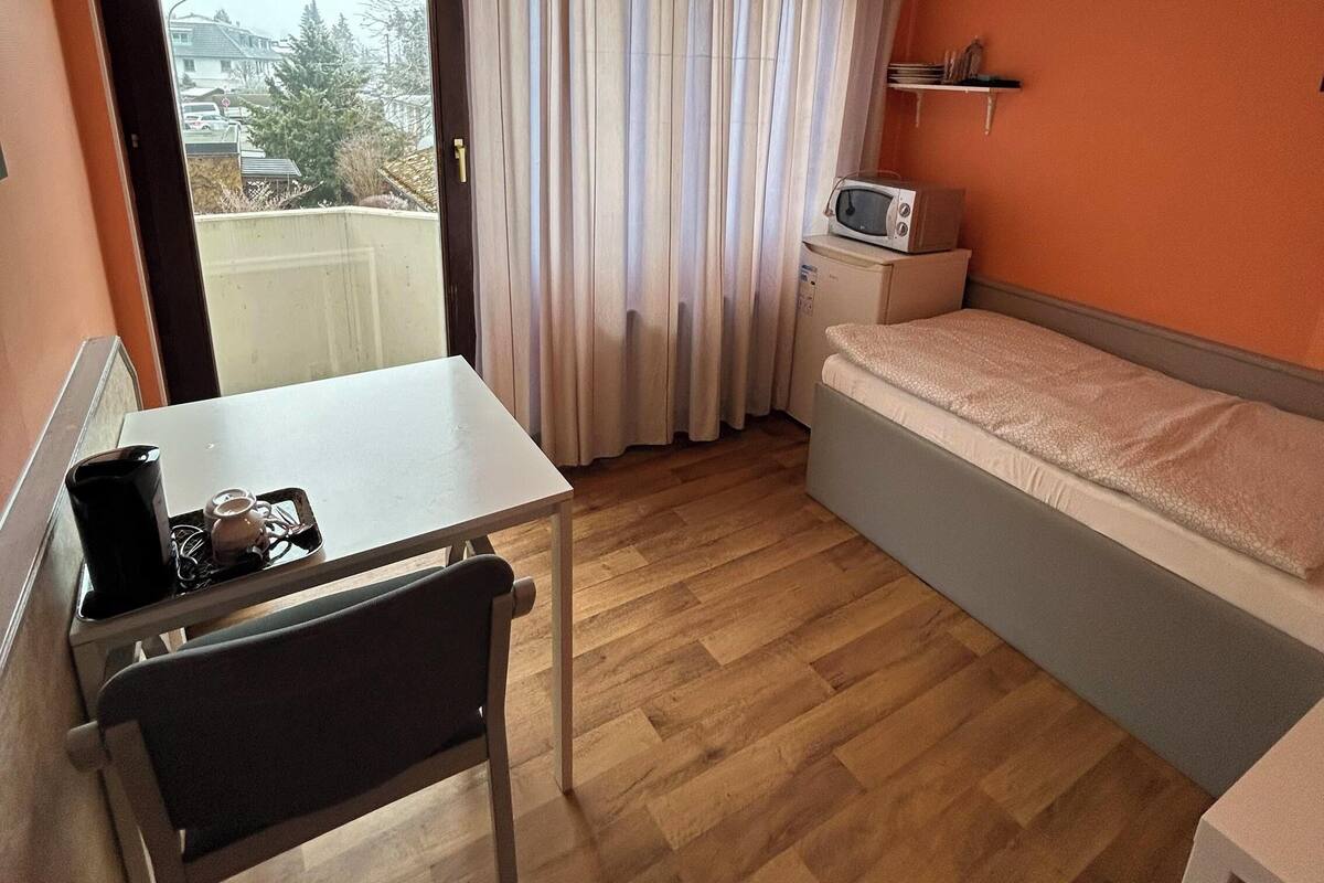 Une petite chambre comprenant un lit, une petite table, un four à micro-ondes et une fenêtre avec des rideaux.